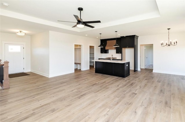 kitchen with a tray ceiling, decorative light fixtures, custom exhaust hood, and a kitchen island with sink