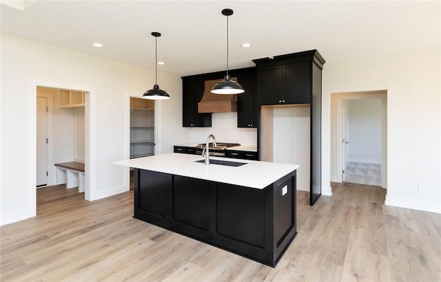 kitchen featuring light hardwood / wood-style flooring, hanging light fixtures, premium range hood, sink, and a kitchen island with sink