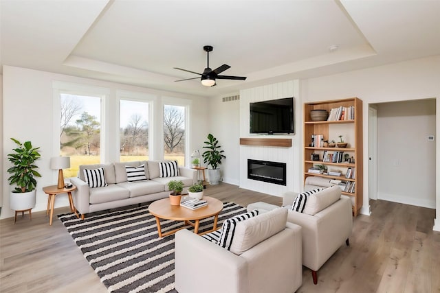 living room with a tray ceiling, light hardwood / wood-style flooring, and a large fireplace