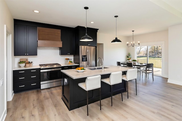 kitchen with premium range hood, stainless steel appliances, an island with sink, decorative light fixtures, and sink