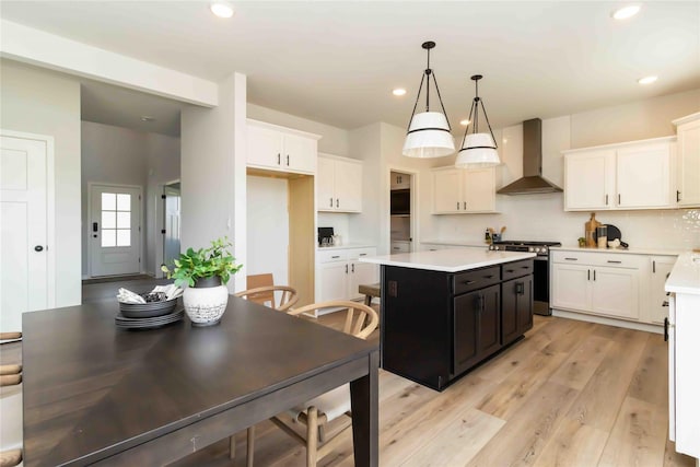 kitchen with stainless steel gas range oven, wall chimney range hood, a kitchen island, white cabinets, and light countertops