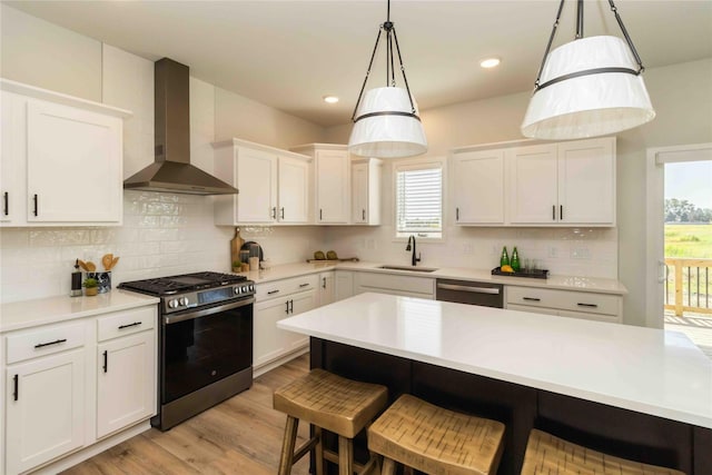 kitchen with a kitchen bar, light wood-style flooring, stainless steel appliances, wall chimney exhaust hood, and a sink