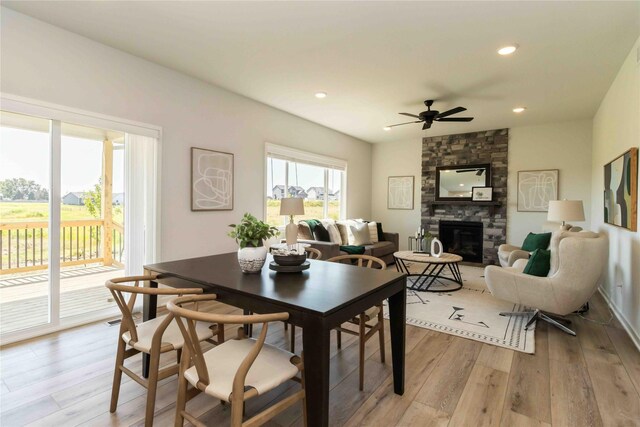 dining space featuring ceiling fan, a stone fireplace, and light wood-type flooring