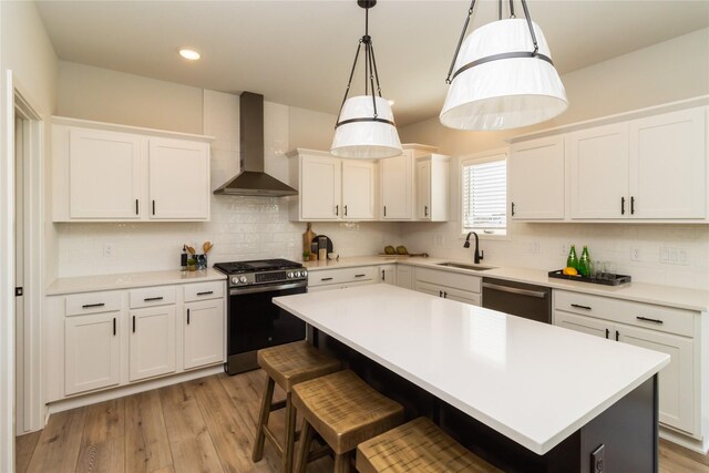 kitchen featuring wall chimney exhaust hood, decorative light fixtures, a center island, and stainless steel gas stove