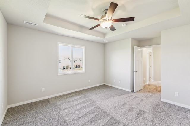 carpeted spare room featuring a tray ceiling and ceiling fan