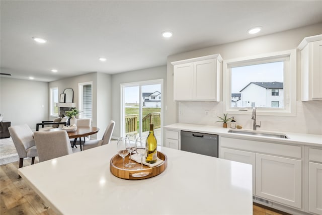 kitchen featuring white cabinetry, sink, backsplash, stainless steel dishwasher, and light hardwood / wood-style flooring