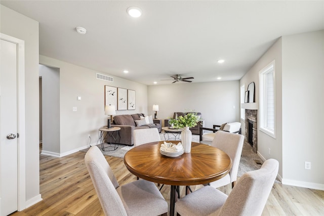 dining space featuring a fireplace, ceiling fan, and light wood-type flooring