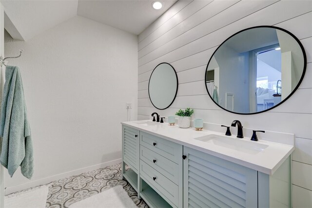 bathroom with vaulted ceiling, vanity, wooden walls, and tile patterned flooring