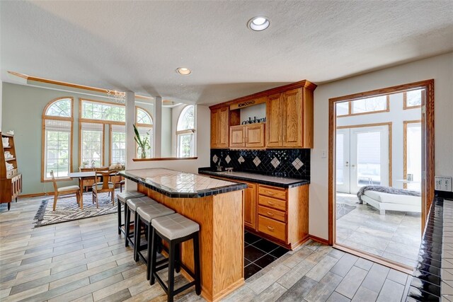 kitchen featuring tasteful backsplash, a textured ceiling, a kitchen breakfast bar, tile countertops, and light hardwood / wood-style floors