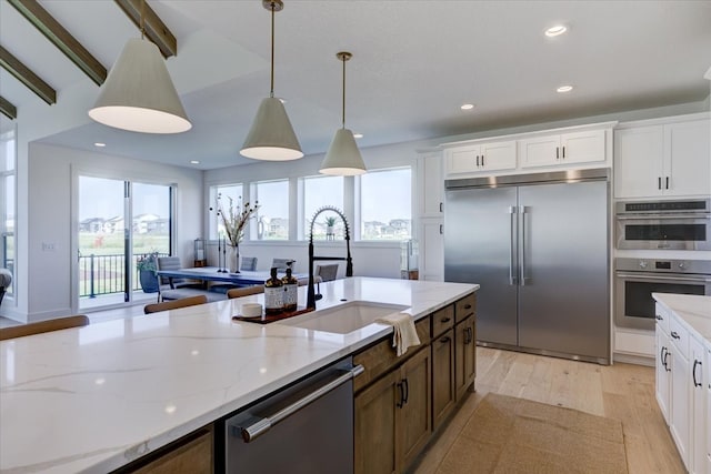 kitchen with stainless steel appliances, hanging light fixtures, white cabinets, and a healthy amount of sunlight