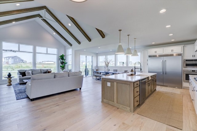 kitchen featuring light hardwood / wood-style flooring, stainless steel appliances, hanging light fixtures, white cabinets, and an island with sink