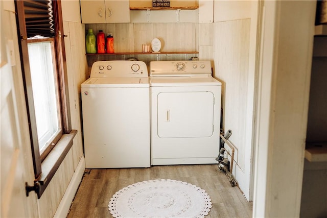 clothes washing area featuring washer and clothes dryer, cabinet space, light wood-style floors, and wooden walls