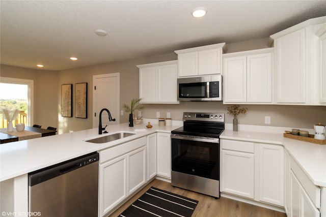 kitchen with kitchen peninsula, white cabinetry, sink, and appliances with stainless steel finishes