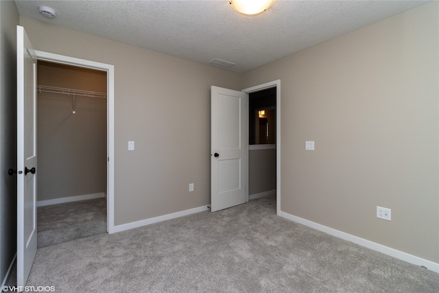 unfurnished bedroom featuring a textured ceiling, light carpet, a walk in closet, and a closet