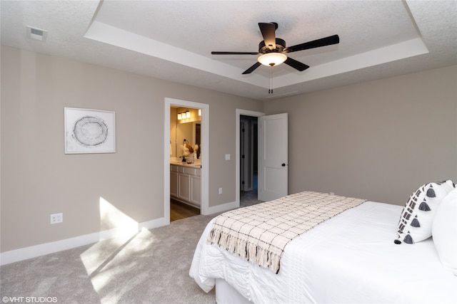 carpeted bedroom with a textured ceiling, ceiling fan, a raised ceiling, and connected bathroom