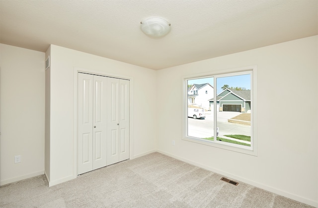 unfurnished bedroom with a closet, light colored carpet, and a textured ceiling