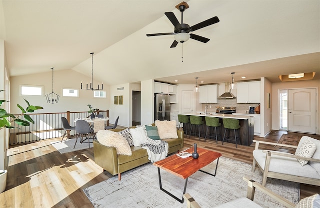 living room with ceiling fan with notable chandelier, light wood-type flooring, lofted ceiling, and sink