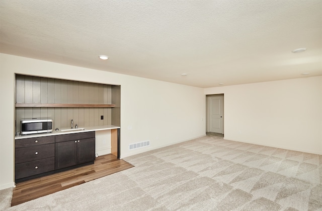 unfurnished living room with a textured ceiling, sink, and light colored carpet