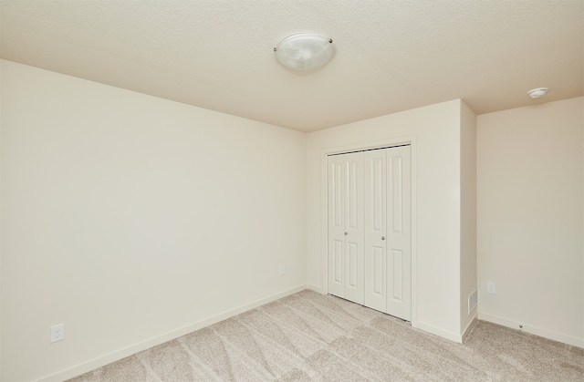 unfurnished bedroom featuring a closet, light colored carpet, and a textured ceiling