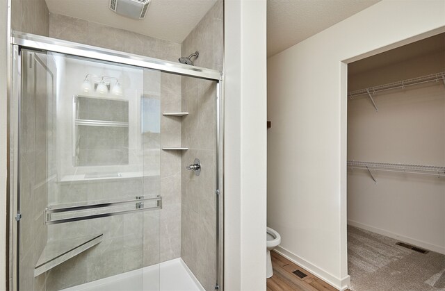 bathroom with a textured ceiling, hardwood / wood-style flooring, walk in shower, and toilet