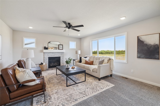 living room featuring ceiling fan, carpet flooring, and a stone fireplace