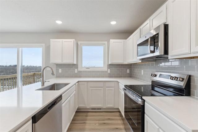 kitchen with white cabinets, appliances with stainless steel finishes, sink, backsplash, and light wood-type flooring