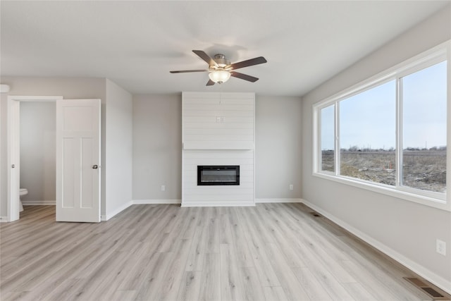 unfurnished living room with a large fireplace, ceiling fan, and light hardwood / wood-style floors