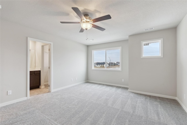 unfurnished bedroom featuring ceiling fan, a textured ceiling, light carpet, and ensuite bath