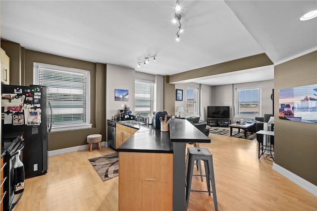 kitchen with a kitchen breakfast bar, light wood-type flooring, a wealth of natural light, and black appliances