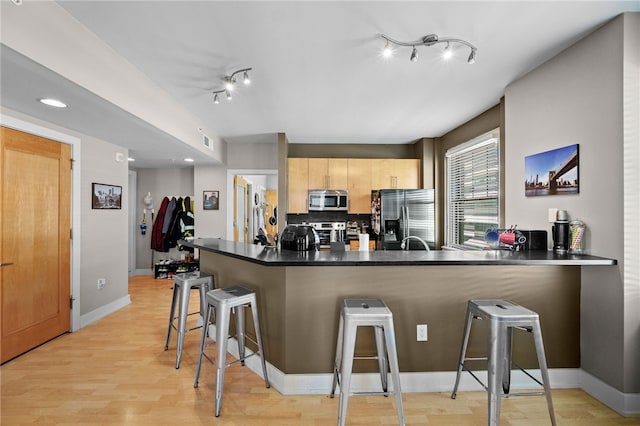 kitchen with a breakfast bar, stainless steel appliances, kitchen peninsula, light brown cabinetry, and light wood-type flooring