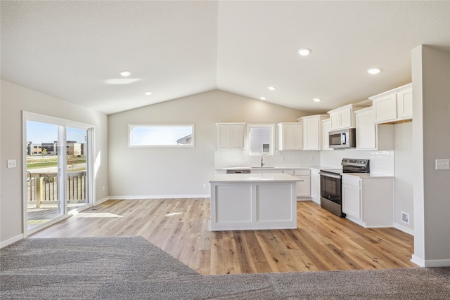 kitchen with lofted ceiling, white cabinets, stainless steel appliances, and light hardwood / wood-style floors