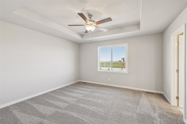 carpeted empty room with ceiling fan and a raised ceiling