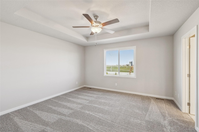 carpeted empty room with a raised ceiling, visible vents, a ceiling fan, and baseboards