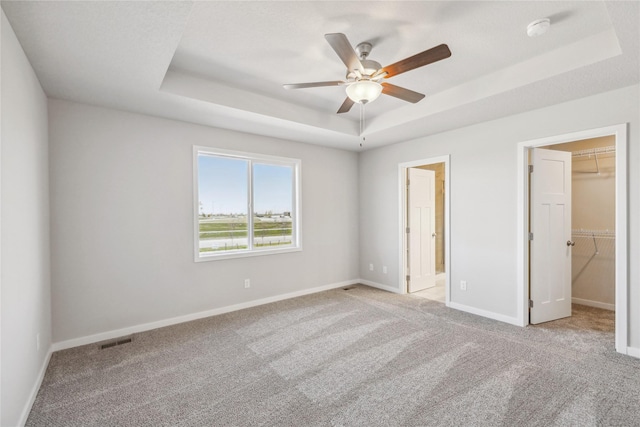 unfurnished bedroom featuring a spacious closet, light carpet, a raised ceiling, baseboards, and visible vents