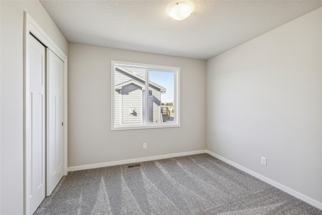 unfurnished bedroom with a textured ceiling, a closet, carpet floors, baseboards, and visible vents