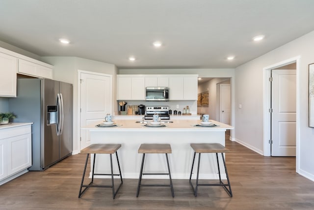 kitchen featuring white cabinets, appliances with stainless steel finishes, dark hardwood / wood-style floors, and a center island with sink