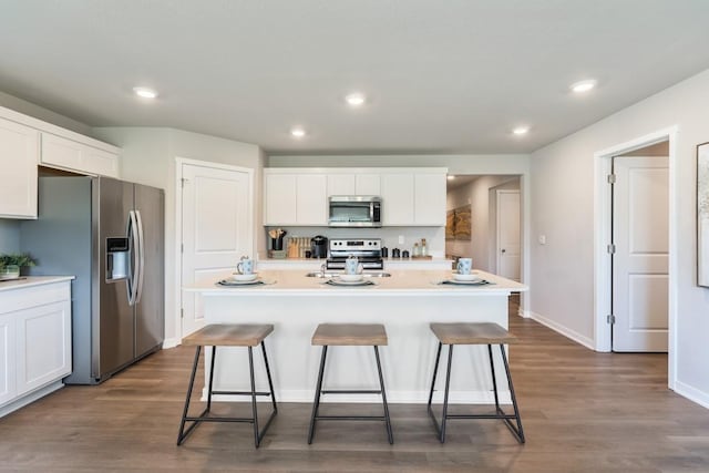 kitchen featuring dark wood-style floors, appliances with stainless steel finishes, a kitchen bar, and white cabinetry