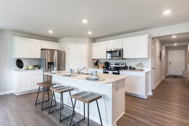 kitchen with a kitchen breakfast bar, a center island with sink, stainless steel appliances, hardwood / wood-style flooring, and white cabinets