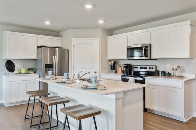 kitchen featuring light wood-style flooring, a kitchen breakfast bar, stainless steel appliances, white cabinetry, and a sink