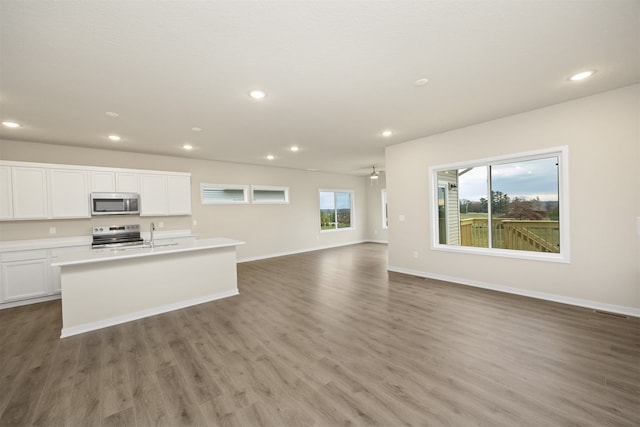 kitchen with hardwood / wood-style floors, white cabinets, a center island with sink, ceiling fan, and appliances with stainless steel finishes