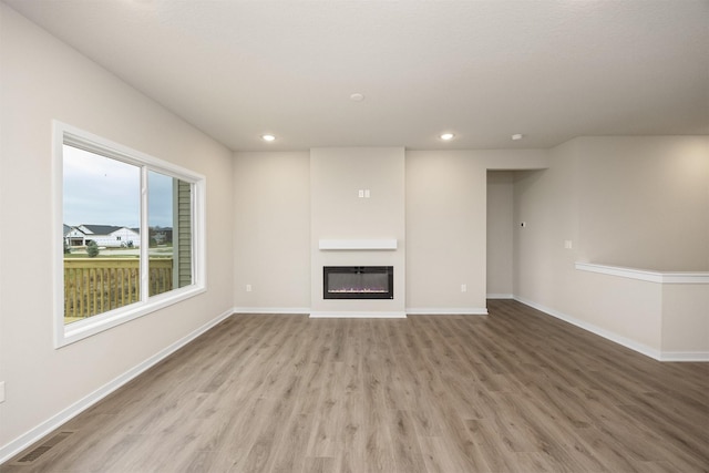 9020 Mockingbird Dr, West Des Moines, IA 50266 - unfurnished living room with light wood-type flooring, recessed lighting, a glass covered fireplace, and baseboards