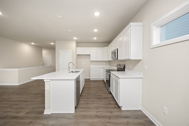 kitchen with dark hardwood / wood-style flooring, stainless steel appliances, sink, white cabinets, and an island with sink