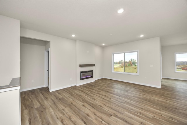 9042 Mockingbird Dr, West Des Moines, IA 50266 - unfurnished living room with wood finished floors, a glass covered fireplace, baseboards, and recessed lighting