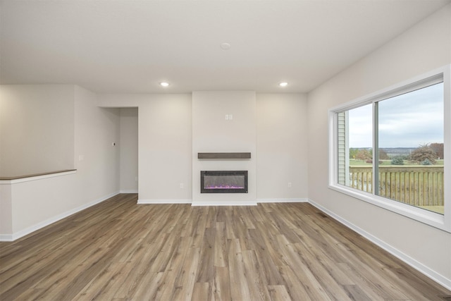 9042 Mockingbird Dr, West Des Moines, IA 50266 - unfurnished living room featuring light wood finished floors, baseboards, recessed lighting, a glass covered fireplace, and heating unit