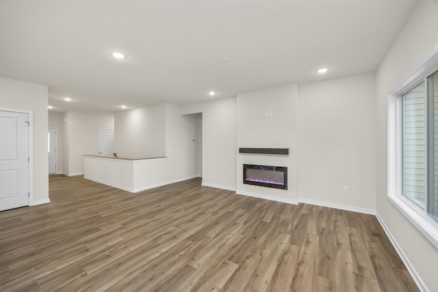 9042 Mockingbird Dr, West Des Moines, IA 50266 - unfurnished living room with light wood-style floors, recessed lighting, a glass covered fireplace, and baseboards