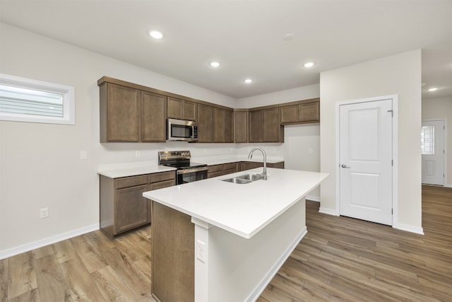 kitchen featuring appliances with stainless steel finishes, an island with sink, light hardwood / wood-style flooring, and sink