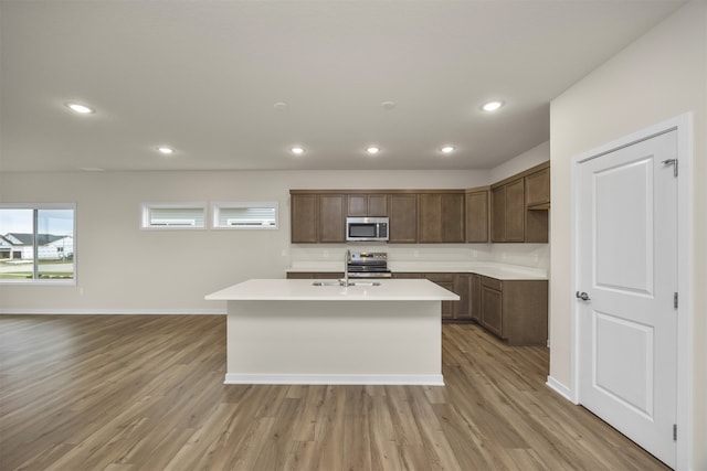 kitchen with appliances with stainless steel finishes, light hardwood / wood-style floors, a kitchen island with sink, and sink