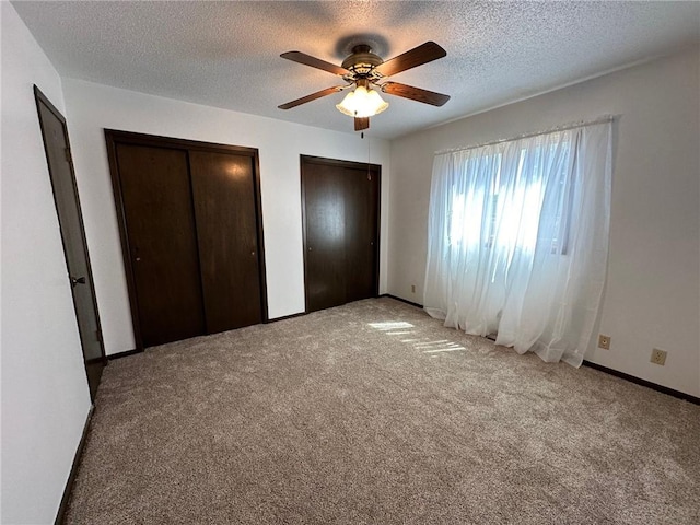 unfurnished bedroom featuring ceiling fan, light colored carpet, a textured ceiling, and two closets