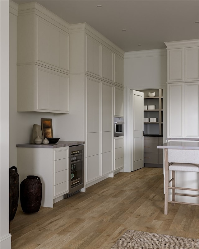 kitchen with white cabinetry, ornamental molding, stainless steel oven, and light wood-type flooring