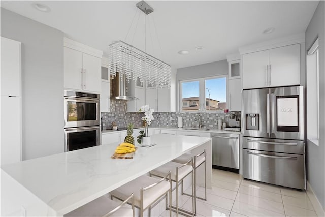 kitchen featuring backsplash, wall chimney range hood, stainless steel appliances, white cabinetry, and a sink